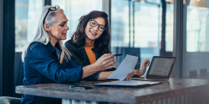 Two women analyzing documents at office Two women analyzing documents while sitting on a table in office. Woman executives at work in office discussing some paperwork.